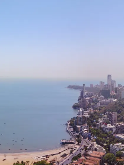 A sweeping drone shot looking down the coastline from Malabar Hill, showing the curve of the bay and the city stretching into the distance.