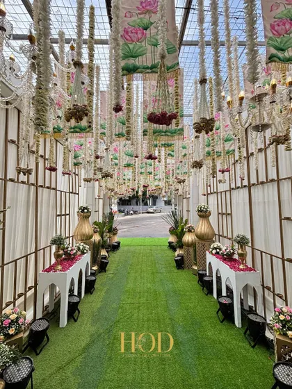 The full length of the green aisle, flanked by traditional decor elements and leading into the venue. The overhead decor with chandeliers and floral hangings makes the entire path a grand statement.