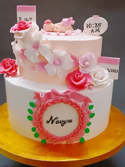A lovely two-tiered welcome cake for baby Navya, decorated with delicate pink and white sugar flowers.