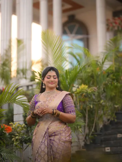 A bride posing in front of a grand building, her purple and gold saree looking regal and elegant.