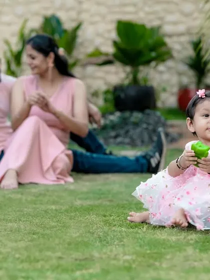 A sweet candid photo from a family session. While her parents relax in the background, this little girl in her pretty pink dress is the star of the show, captured in our green garden.