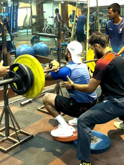 Coaching a heavy back squat with an athlete using heel elevation to improve depth and posture. My hands-on approach ensures that even during maximal effort lifts, technique is never compromised.
