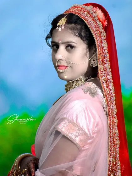 A classic portrait of a bride, her red dupatta framing her face beautifully against a bright blue sky.