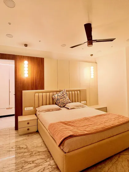 This bedroom design focuses on a soothing, neutral palette of beige, white, and wood. The upholstered headboard and warm pendant lights create a cozy and inviting atmosphere, while the wood paneling adds texture and warmth.