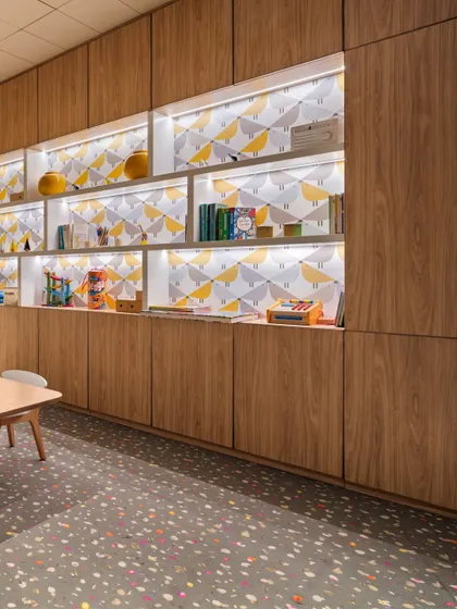 The kids' play area at the Elevate Clubhouse features cheerful wallpaper and custom wood cabinetry with integrated lighting. We added windows to what was initially a closed-off space to bring in natural light and create a bright, engaging environment.