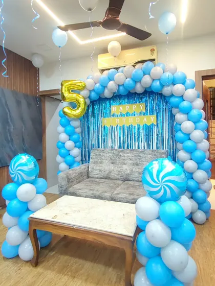 A classic blue and white balloon arch for a 5th birthday. This home setup includes a shimmer curtain backdrop, a 'Happy Birthday' banner, and two candy-swirl foil balloons on pillars.