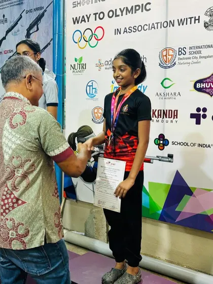 A young shooter receives her medal and certificate from an esteemed guest during our Best Shot Open Competition, recognizing her hard work and performance.