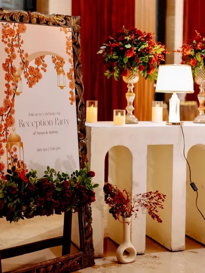 The elegant welcome sign for the reception, set in a carved wooden frame and surrounded by beautiful red floral arrangements.