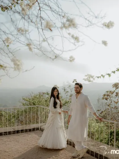 A beautiful portrait of a couple on a balcony with white flowers overhead and a hazy mountain view behind them. The image feels calm, airy, and deeply romantic.