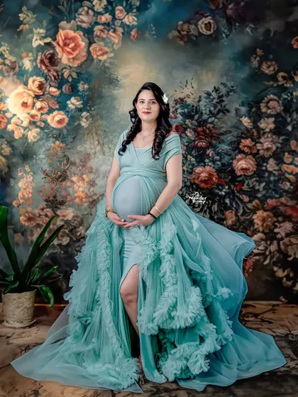 A fine art portrait against a painted floral backdrop. The flowing teal gown and artistic setting give this image the quality of a classical painting.