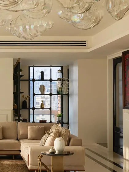 A secondary seating area in the South Bombay home, featuring a neutral L-shaped sofa and a custom black shelving unit. The large windows frame the city view, making it a perfect spot to relax and unwind.