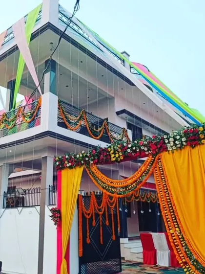 A grand entrance decoration for a wedding house. The gate is decorated with a large arch of yellow and pink drapes and flowers, and the house facade is also adorned with colorful fabric.
