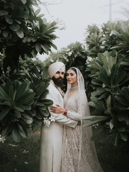 A beautiful couple portrait amidst lush greenery. The natural setting provides a stunning contrast to their elegant white wedding attire.