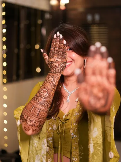 A happy smile and a hand full of henna. This bride is playfully showing off her full-arm mehendi, a beautiful mix of traditional patterns and personalized story elements.