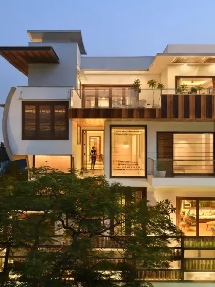 The illuminated façade of the Ashraya Residence at dusk highlights its layered volumes and the warm glow from within. The design balances transparency with privacy, creating a welcoming beacon in the neighborhood.