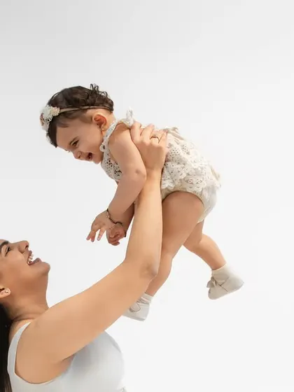 A mother joyfully lifts her baby in the air. The baby's delighted expression and the mother's smile make this a perfect capture of pure happiness.