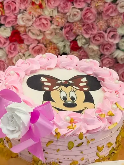 A sweet and simple Minnie Mouse photo cake. The pink frosting, bow, and pistachio details make it a charming choice for a Disney-themed party.