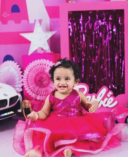 Welcome to the Barbie dream house. This little girl is shining in her sparkly pink dress, surrounded by balloons and her favorite dolls.