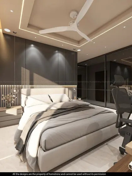 A bedroom with a mirrored wardrobe that visually doubles the space. The design includes a study desk and a bed with a simple, clean-lined headboard.