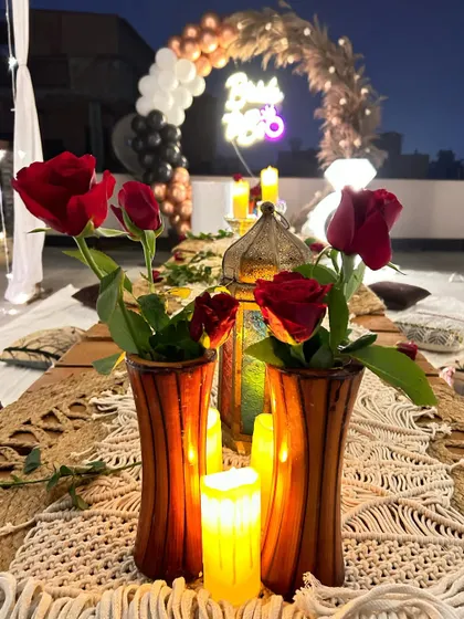 A close-up of the romantic terrace table setting. The decor features red roses, candles, and macrame table runners, creating an intimate and special ambiance.