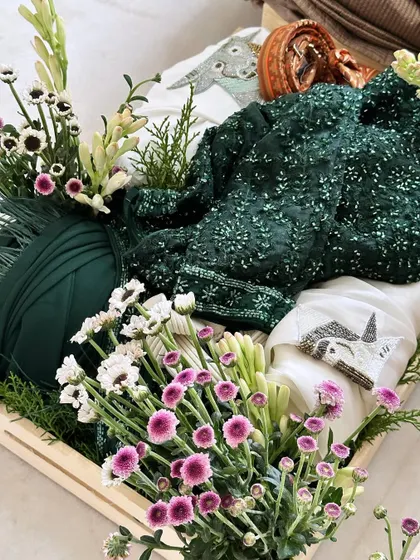 A tray featuring a dark green sequined outfit, beautifully contrasted with fresh white and purple flowers. A perfect gift for a sangeet or reception.