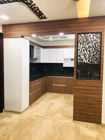 A U-shaped kitchen framed by a wooden partition with an intricate jali panel. This is a great way to add a traditional Indian design element to a modern home.
