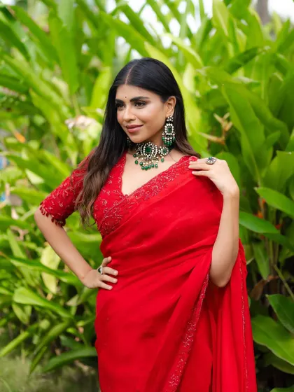 A confident pose that showcases the stunning emerald jewelry against the red saree. The contrast is striking and beautiful.