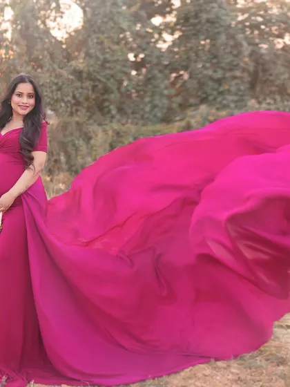 A dramatic outdoor shot featuring a vibrant pink gown with a long, flowing train tossed in the air. This adds a dynamic and high-fashion element to the maternity session.