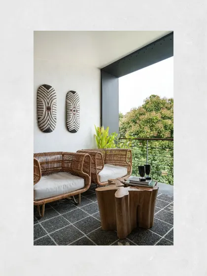 A cozy seating nook on a balcony at Kamala Residence, where cane chairs and a live-edge stump table create a perfect spot to enjoy the view of the surrounding trees.