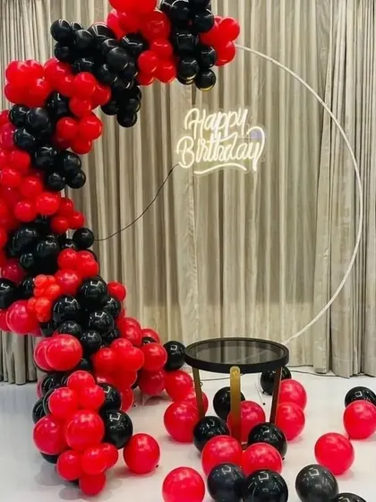 A bold red and black balloon arch on a circular frame with a neon sign.