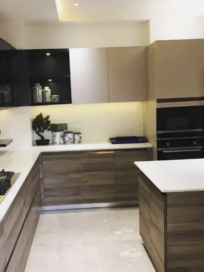 This U-shaped kitchen in Lajpat Nagar combines warm wood-grain lower cabinets with beige upper cabinets. The design includes a small, movable island for flexible workspace and is equipped with built-in appliances.