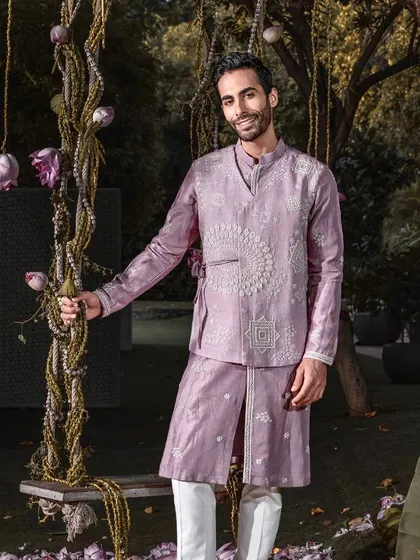 A smiling model wears the contemporary mauve kurta set, featuring an embroidered, overlapping panel. This ensemble radiates grace and grandeur for any celebration.
