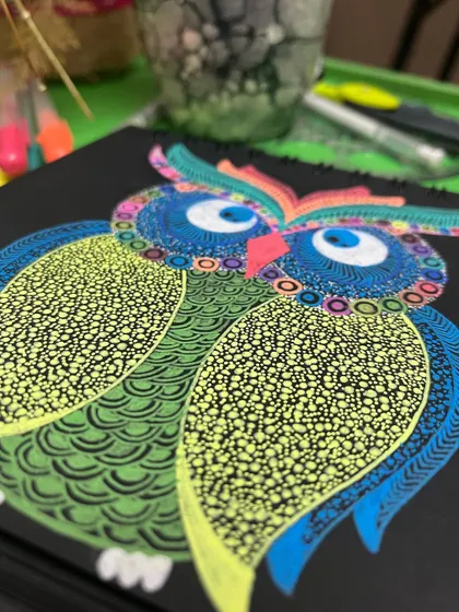 A close-up of a colorful owl doodle on black paper.