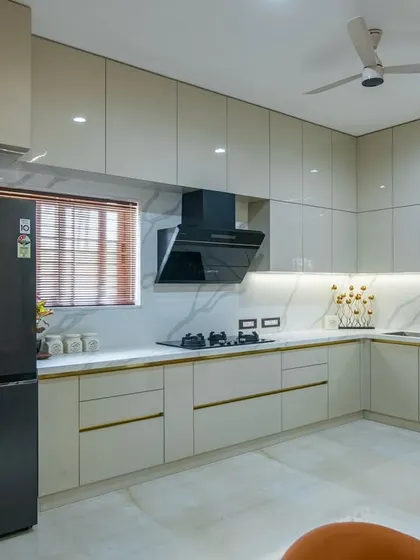 A wide shot of the modern kitchen, featuring light-colored glossy cabinets, a marble-look backsplash, and a black chimney. The design is clean, bright, and highly functional.