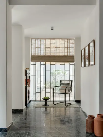 A quiet nook in a hallway, featuring a modern chair and a large window with a geometric grille. This space demonstrates our belief that even transitional areas can be designed as moments of pause and beauty.
