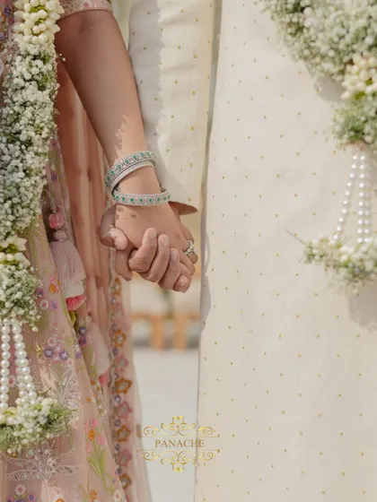 A close-up shot of the couple holding hands, a simple yet powerful symbol of their union. The details of their outfits and the floral garlands are beautifully captured.