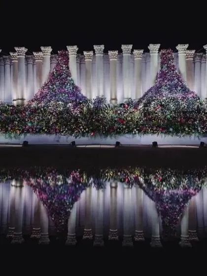 The reflection of the Roman pillars and floral mountains in the water creates a perfectly symmetrical and artistic visual, doubling the impact of the grand design.