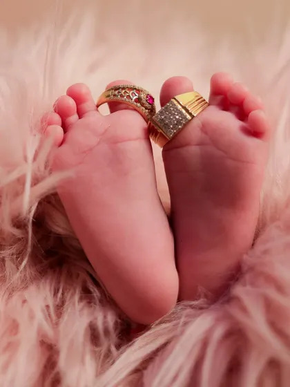 A creative and symbolic shot of a newborn's feet adorned with their parents' wedding rings, signifying the new family bond.