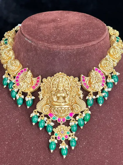 A stunning temple choker with a central Lakshmi motif and green bead drops. The pink kemp stones add a beautiful contrast.