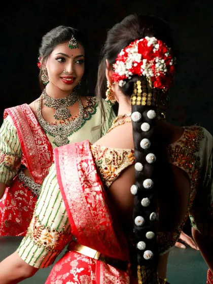 A creative portrait where the bride looks at her reflection. This shot offers two perspectives, showcasing both her smiling face and the intricate details of her traditional hairstyle and saree.