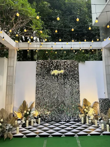 A stunning stage setup for a glamorous cocktail party, featuring a shimmering silver sequin backdrop, a checkerboard floor, and elegant arrangements of pampas grass and white flowers.