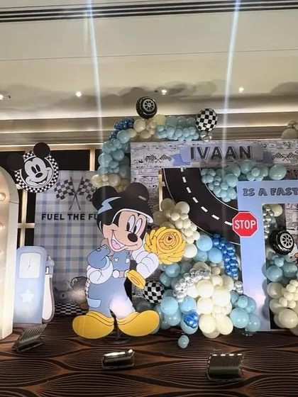 A full stage setup for a Mickey Mouse racing theme, combining character cutouts, a racetrack backdrop, and checkered flag details.