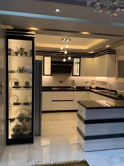 This black and white kitchen features a tall, illuminated glass cabinet for crockery display. The clean lines and contrasting colors create a bold and sophisticated look.