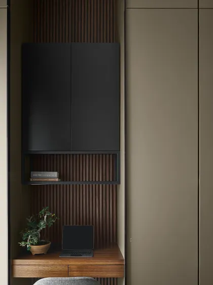 A compact study nook is integrated into the Taupe Bedroom, featuring a teak desk and a black cabinet set against a fluted wood backdrop. This creates a functional workspace without cluttering the room.