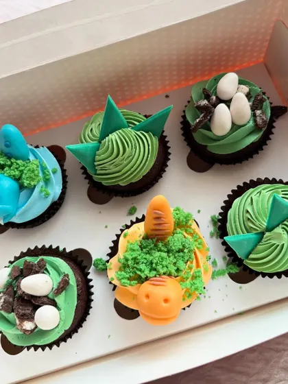 A box of dinosaur-themed cupcakes for a birthday celebration. I used a mix of buttercream piping and fondant details to create little dinos, nests with eggs, and textured green frosting.