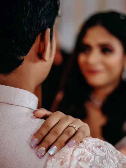 An over-the-shoulder shot that creates a sense of intimacy, focusing on the bride's hand on her fiancé's shoulder, her ring sparkling.