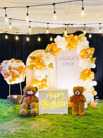 An outdoor Teddy Bear picnic theme for a first birthday, with two large teddy bears and a neon 'Happy Birthday' sign.