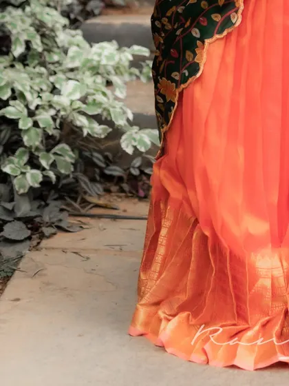 A detail shot of the hem of the metallic orange pleated skirt, showing the rich texture and traditional golden border.