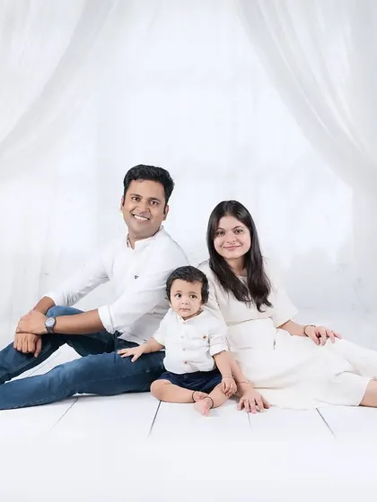 A relaxed family portrait in coordinated white and denim outfits. The family sits together on a white wood floor, creating a casual and timeless look.