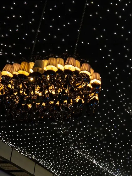 A grand chandelier with individual lampshades hangs beneath a ceiling of fairy lights, creating a dramatic and luxurious focal point.